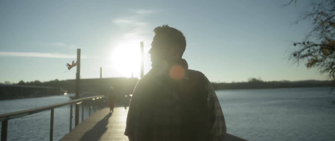The sun shines on a man standing on a pier
