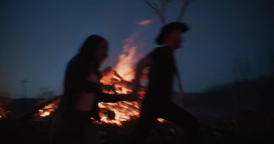Man and woman running through a forest at night with flames of fire
