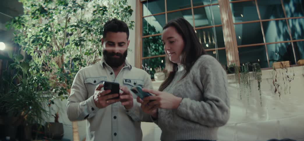 A man and woman are using cell phones side by side