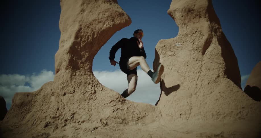 A man is running through the desert and jumps through a rock archway