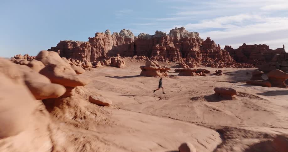 Person running over arid rocky terrain with rock formations and clear sky in the background
