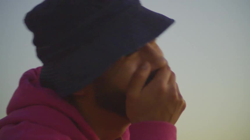 A bearded man in a blue hat and pink sweater laughs loudly