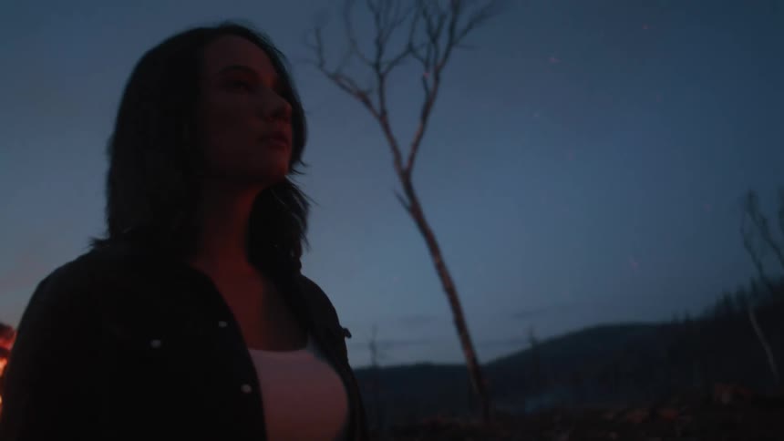 Woman walks away from a bonfire in the evening while smoke rises from the ground in the background