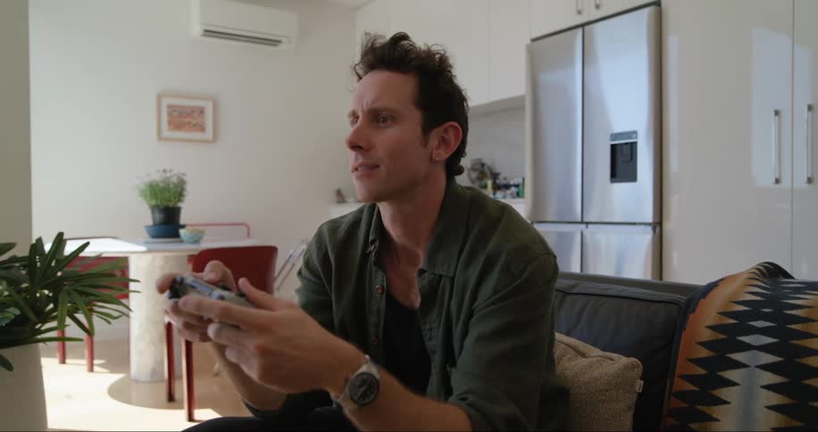 A man is sitting on a couch in a modern living room playing a video game