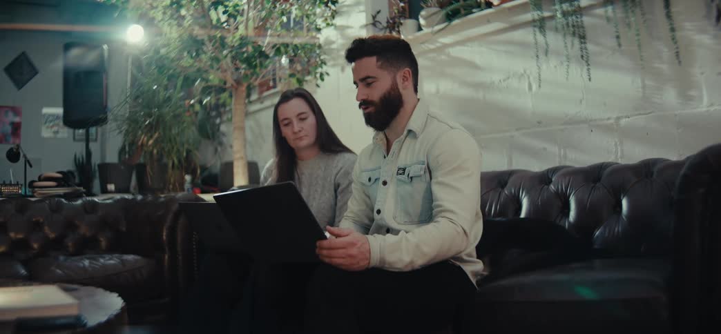 Two people sitting on a couch consult a laptop during a discussion