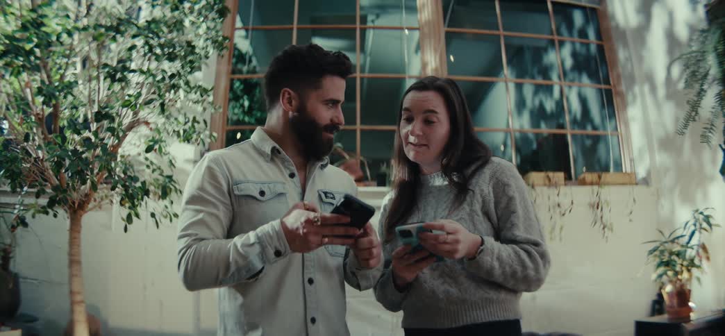 Man talking to a woman indoors illustrates his point with his smartphone