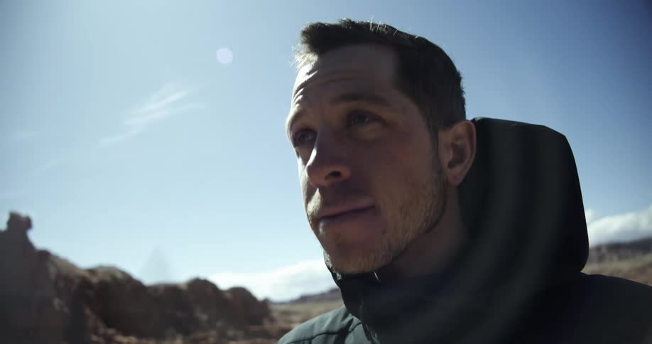 Man standing near a hill in arid terrain on a sunny day removes his sunglasses
