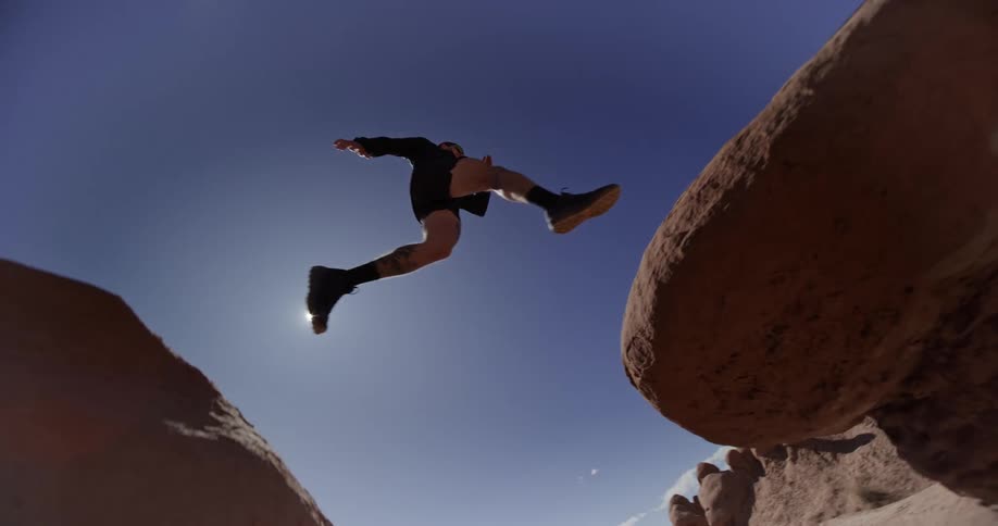 Man jumps between rock formations in arid terrain on a sunny day