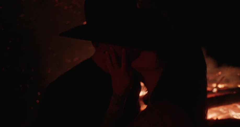 Woman walking towards man to make out in front of large bonfire at night
