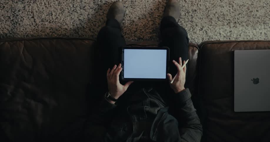 A person sitting on a sofa and using a tablet with a white screen