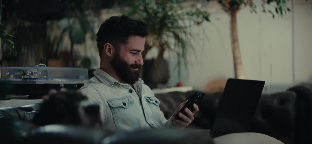 Man sitting interacting with a smartphone and petting a dog next to him at the same time