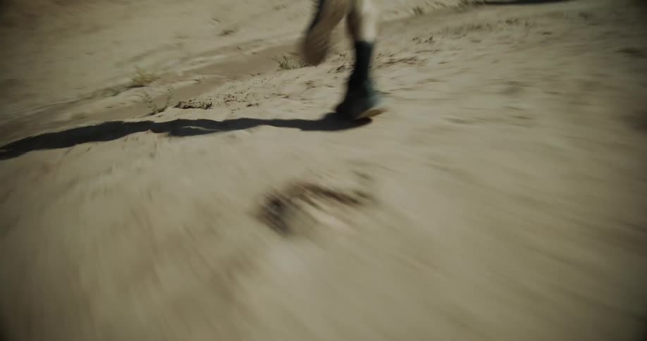 A person is running in a desert landscape with rock formations in the background under a clear blue sky