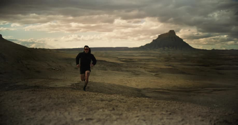 A desert landscape is shown under an overcast sky with the implied movement of someone running offscreen to the right