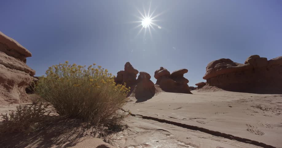 Desert landscape with rock formations and the sun highlighted against a clear blue sky