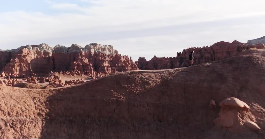 Runner runs along a ridge overlookinga rock formation filled valley on a cloudy day