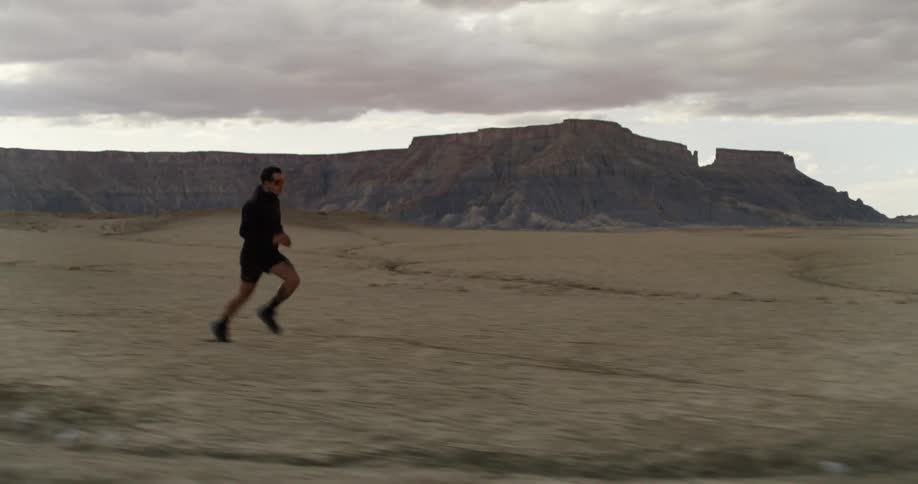 A person is running in a desert landscape with rugged hills in the background under a partly cloudy sky