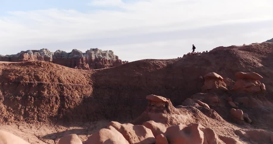 An adult is running along a ridgeline in a desert with large rock formations