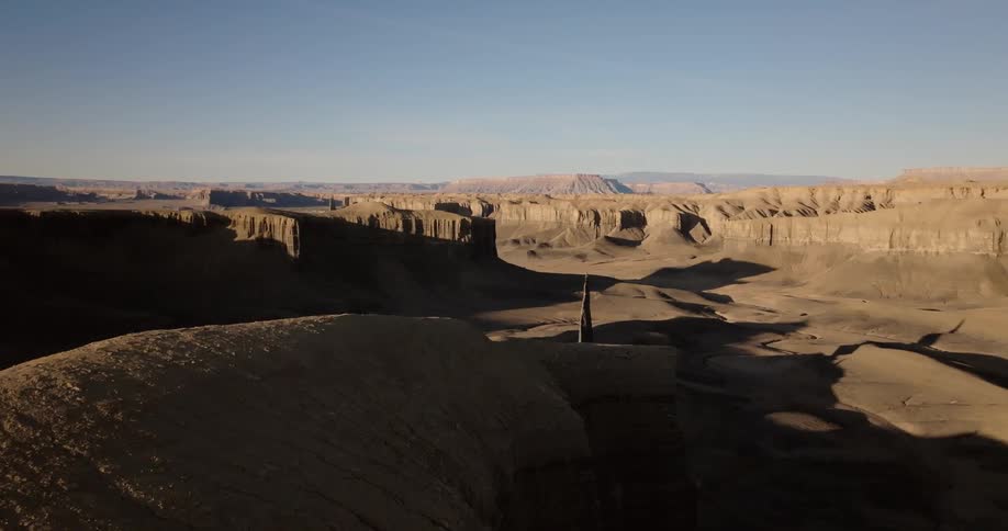 A vast aerial view of a canyon landscape showcases dramatic shadows and towering rock formations under a clear sky