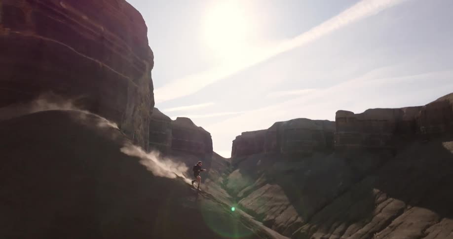 Person running downhill through a desert landscape surrounded by rocky mountains