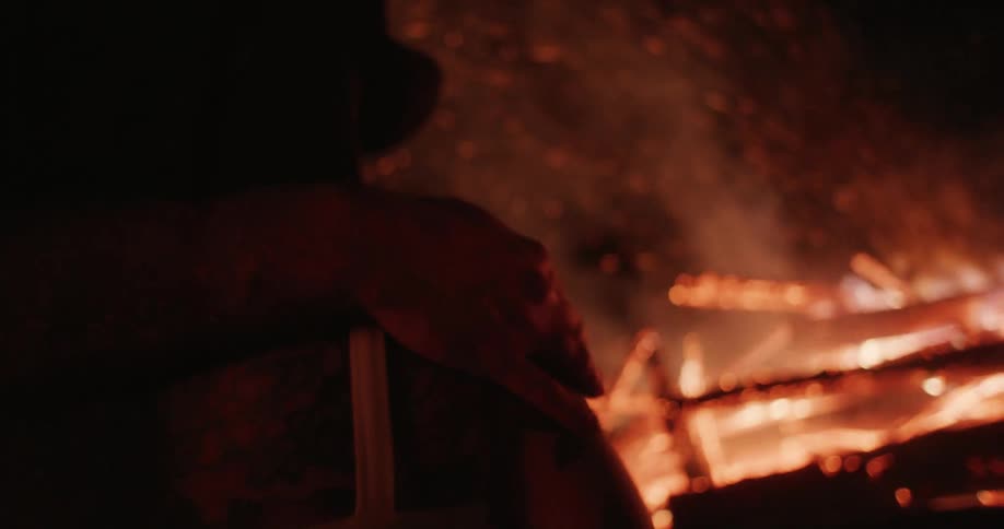 A couple embraces near a large bonfire at night