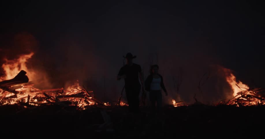 Silhouette of two people holding hands running from an active fire area at night