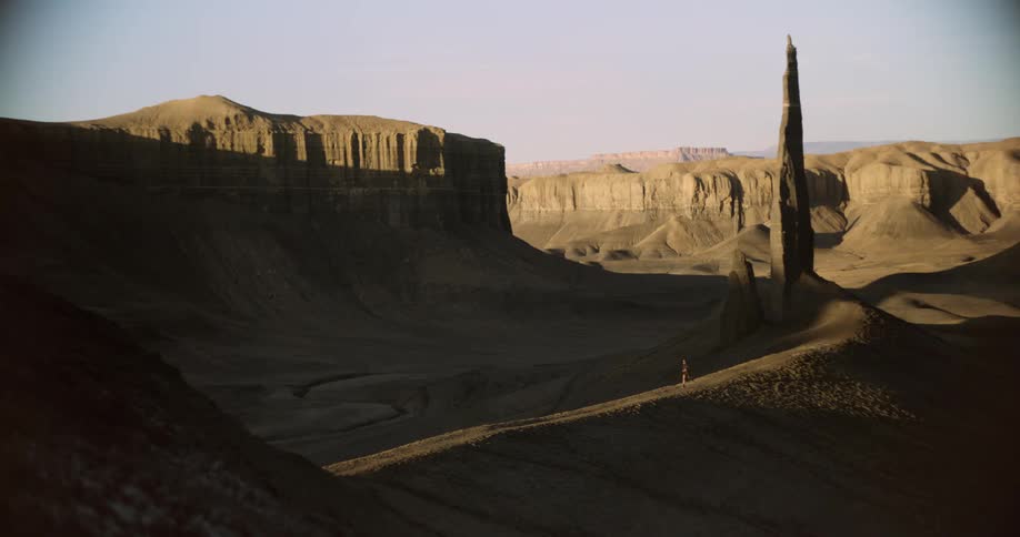 A lone jogger runs along a path in a vast shadowed desert landscape with towering rock formations