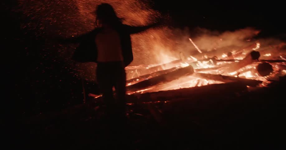 Silhouette of a woman dancing in front of a large bonfire at night