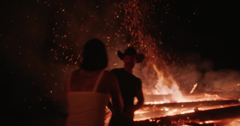 Couple dancing and kissing in front of a bonfire at night