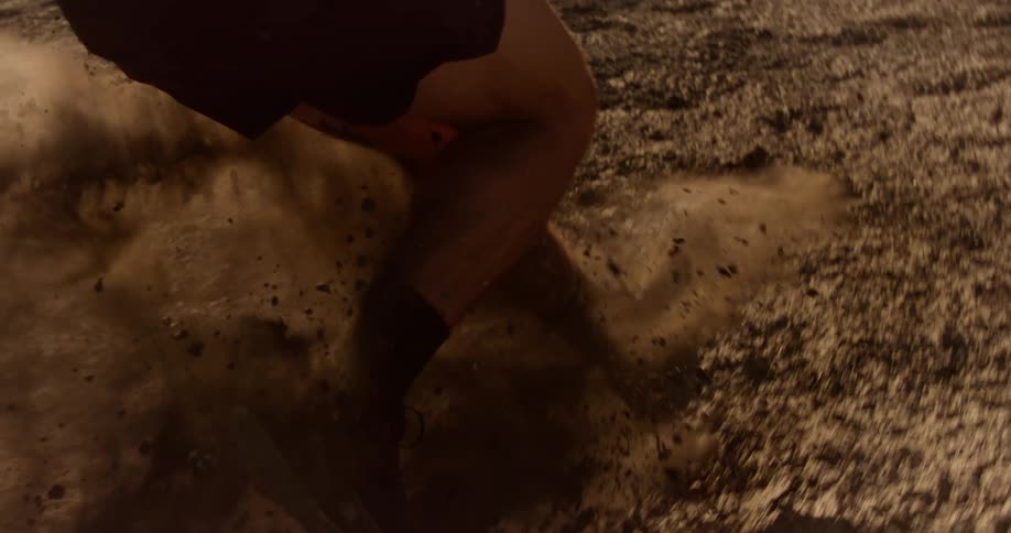 A person runs down a dry hill in a desert landscape kicking up gravel