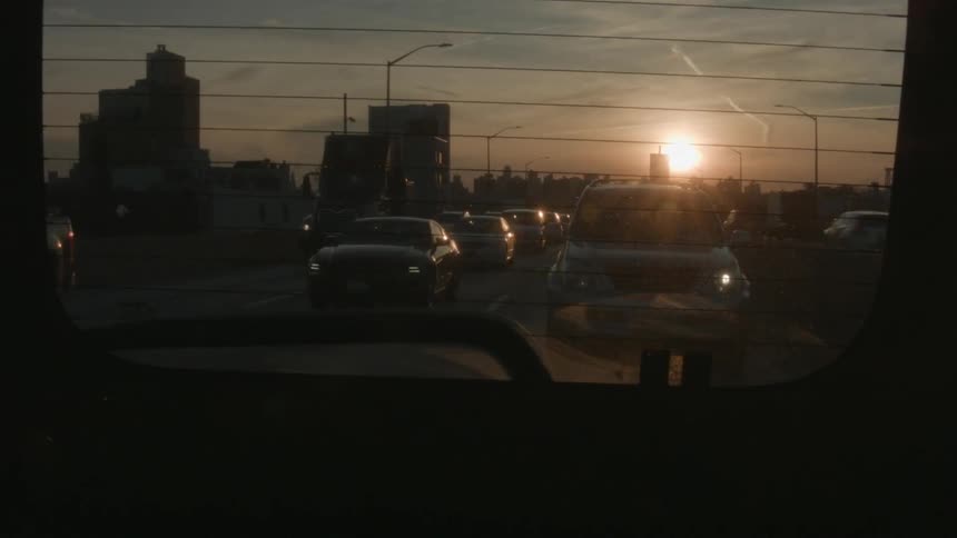 Cars driving on a busy street with sun setting in the distance