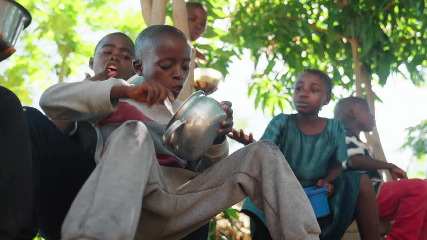 Boys sitting outdoors under a tree eating from pots