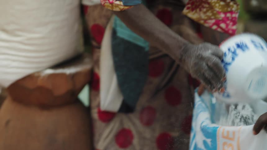 Pair of hands picking up wheat flour and putting it in a bag with the help of a jar