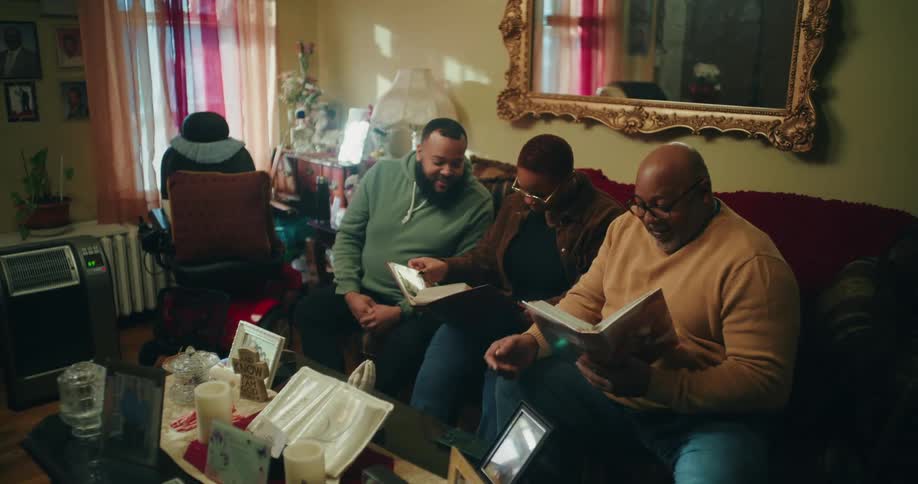 A family sits closely together on a couch looking at photo albums or books in a warmly lit room