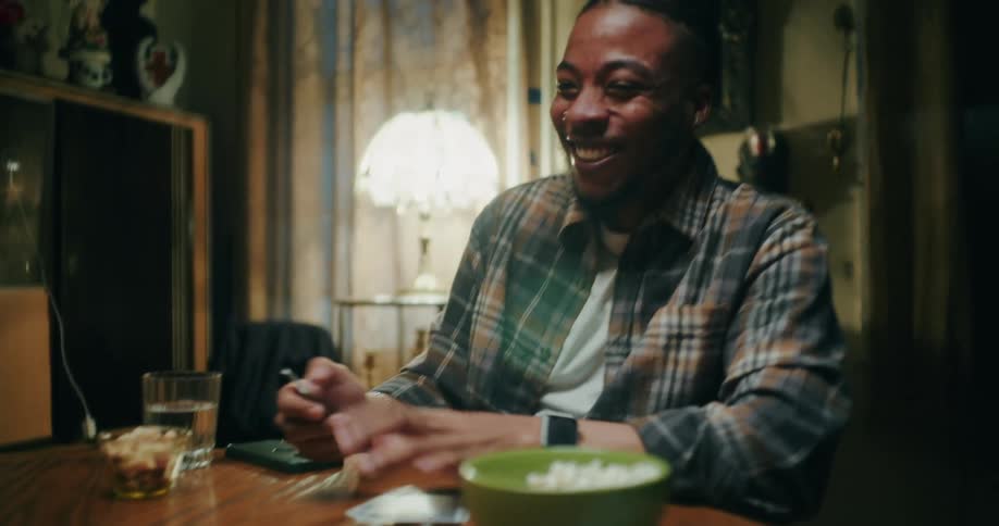 Three friends are laughing and playing cards while sitting indoors at a wooden table
