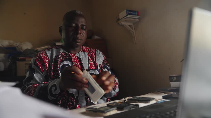 Man sitting at a table in front of an open laptop and taking out a cell phone from a package