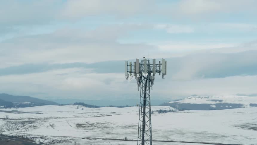 A tall cellular tower works over the snowy terrain of a rural landscape on a winter day