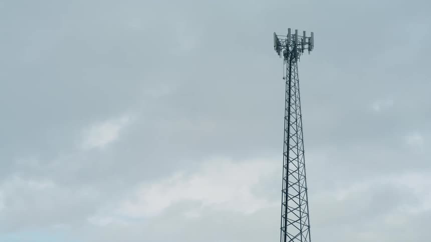 A very tall network transmission tower stands against a partly cloudy sky