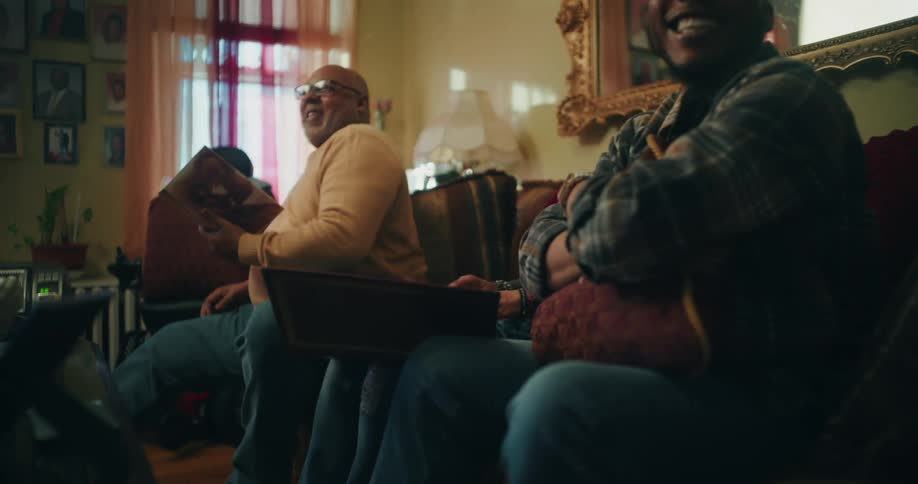 A family sits closely together on a couch looking at photo albums or books in a warmly lit room