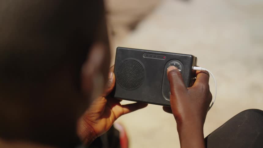 A person is holding a small black portable radio with a control panel and a connected white cable