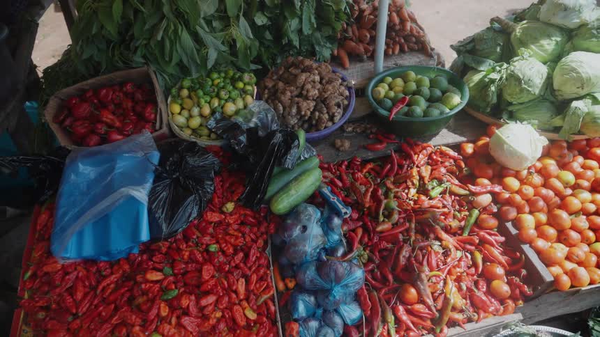 A market stall displaying a variety of fresh produce including red and green chili peppers tomatoes limes leafy greens and other vegetables arranged in baskets and on a table