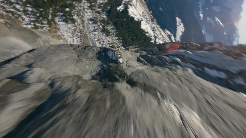 Close aerial gliding along and over a gray rocky cliff slightly covered in snow on a bright day in Switzerland