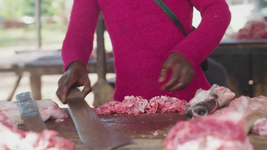 Hand with a knife cutting pieces of fresh meat on a wooden table
