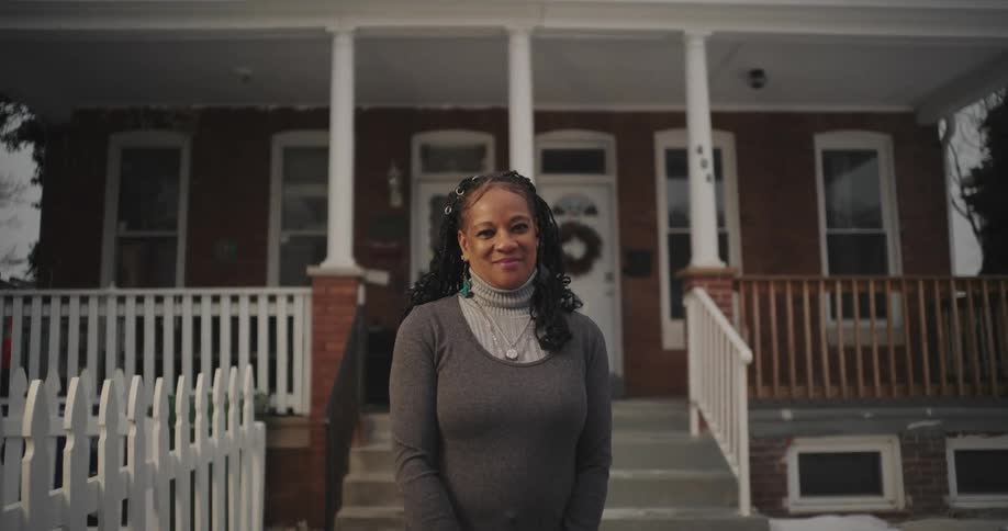 A woman smiles while standing by her home