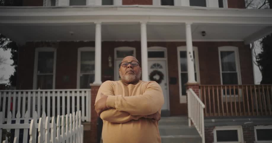Bearded man crossing his arms in front of a house