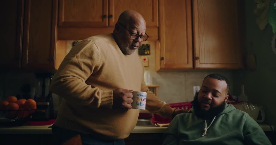 A man sitting down talking to a man standing next to him and holding a white mug