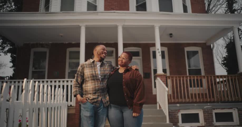A brother and sister are smiling and hugging in front of the house