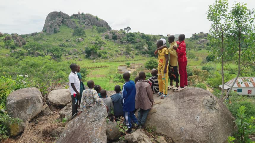 People standing on large rocks point at the mountain in the distance