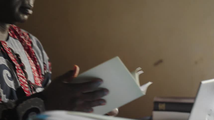 The face of a man who is leafing through a paper in his hand and in front of him there is a laptop