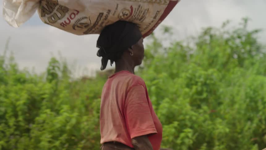 Woman walking and carrying a full bag on her head
