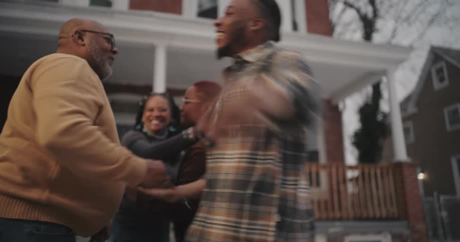 A family greet each other and hug in front of the house